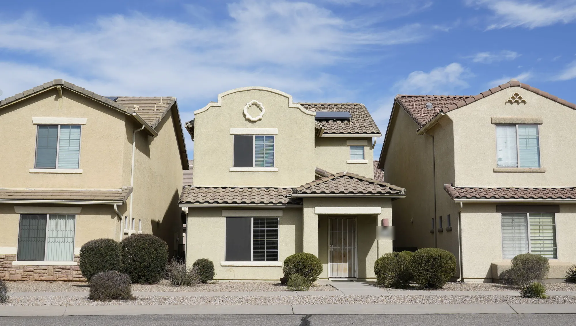 Two-storey stucco houses with clay tile roofs and gravel desert landscaping under a hard blue Arizona sky